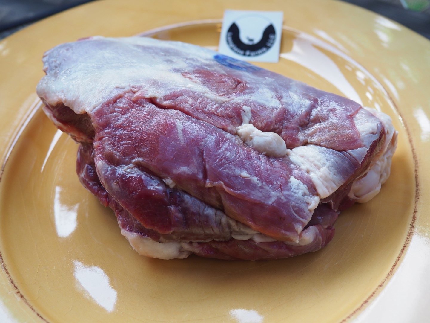 A Kiko goat roast on a yellow plate beside the Longlane Farms logo.