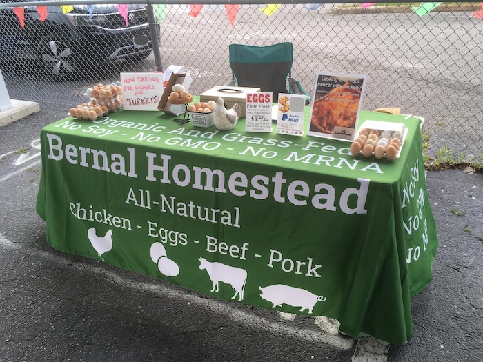 A farmers market table with the green Bernal Homestead cloth displaying eggs and signage.