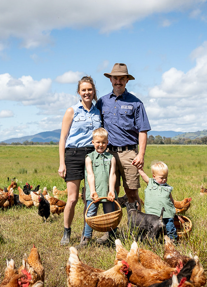 Family standing in an open field surrounded by free-range chickens.